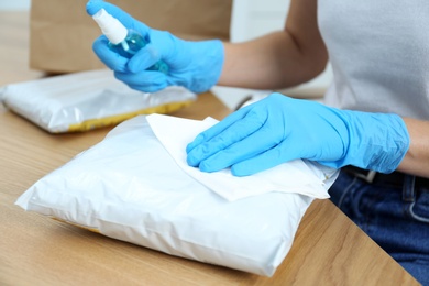 Woman cleaning parcel with wet wipe and antibacterial spray at wooden table, closeup. Preventive measure during COVID-19 pandemic