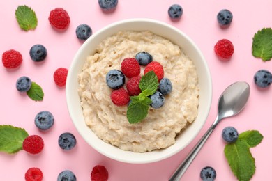 Photo of Tasty oatmeal porridge with raspberries and blueberries in bowl on pink background, flat lay