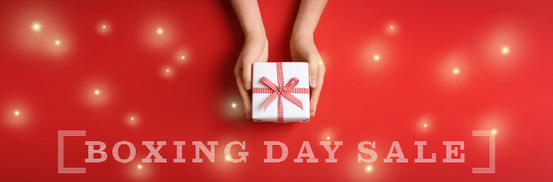 Boxing day sale banner design. Woman holding gift on red background, top view