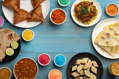 Frame of traditional Indian food and color powders on light blue wooden table, flat lay with space for text. Holi festival celebration