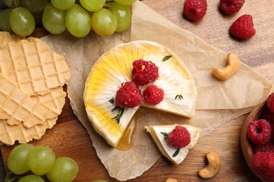 Brie cheese served with berries and honey on wooden table, flat lay