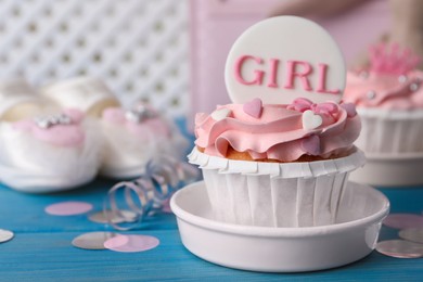 Photo of Delicious cupcake with pink cream and Girl topper for baby shower on light blue wooden table, closeup