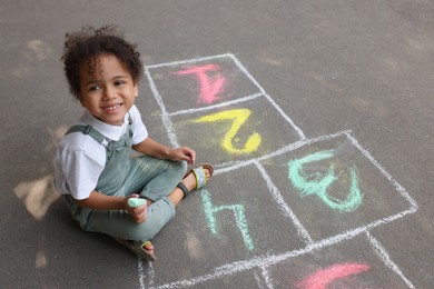 Little African American girl drawing hopscotch with chalk on asphalt outdoors. Happy childhood