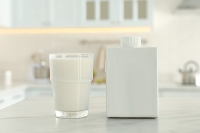 Photo of Carton box and glass of milk on table in kitchen