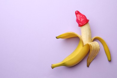 Banana with condom on lilac background, top view and space for text. Safe sex concept