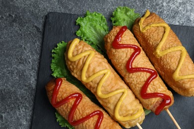 Delicious deep fried corn dogs with lettuce and sauces on grey table, top view