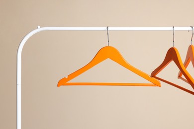 Photo of Orange clothes hangers on metal rack against beige background