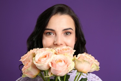 Young woman with beautiful bouquet on purple background