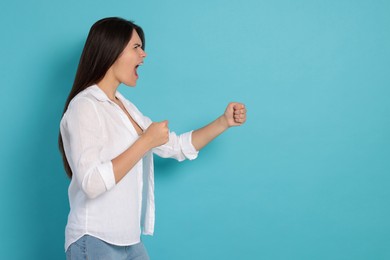 Aggressive young woman shouting on turquoise background, space for text
