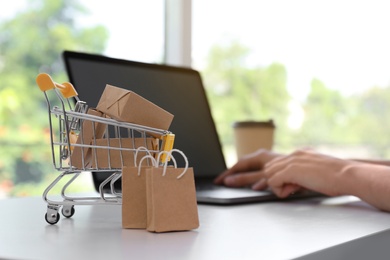 Internet shopping. Small cart with boxes and bags near woman using laptop indoors