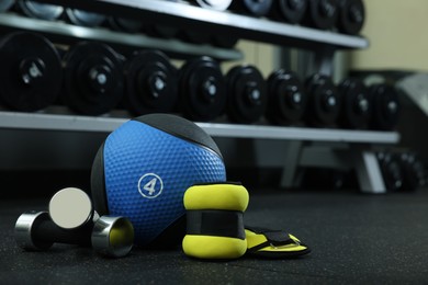Blue medicine ball, weighting agents and dumbbells on floor in gym, space for text