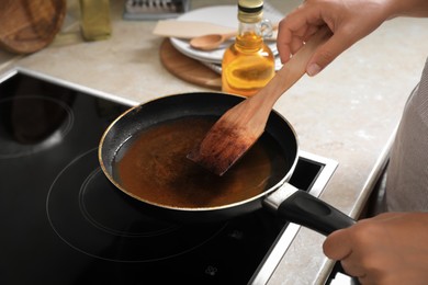 Photo of Woman with wooden spatula and frying pan of used cooking oil near stove, closeup