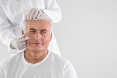 Doctor examining senior man face before cosmetic surgery on white background. Space for text