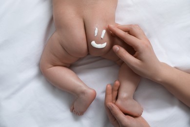 Mother applying body cream on her little baby, top view