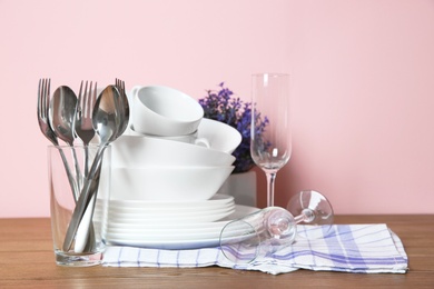Set of clean dishes and cutlery on table against color background