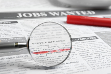 Looking through magnifying glass at newspaper, closeup. Job search concept