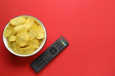 Remote control and bowl of potato chips on red background, flat lay. Space for text