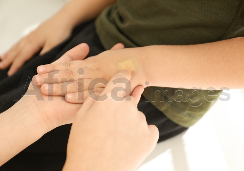 Photo of Sister putting sticking plaster onto little brother's hand indoors, closeup