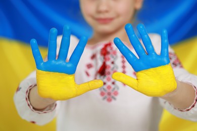Photo of Little girl with painted hands near Ukrainian flag, closeup. Love Ukraine concept