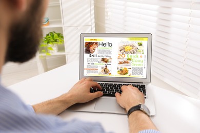 Man reading online magazine on laptop at white table, closeup