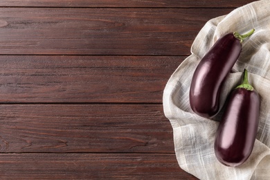 Ripe purple eggplants and napkin on wooden table, top view. Space for text