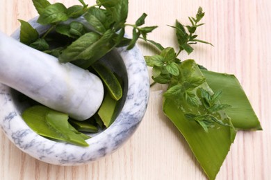 Mortar with pestle, aloe and mint leaves on wooden table, top view