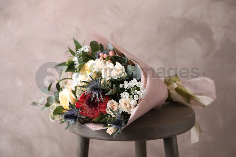 Beautiful bouquet with roses on chair near beige wall