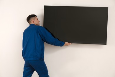 Professional technician installing modern flat screen TV on wall indoors