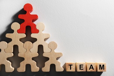 Photo of Red figure among wooden ones and cubes with word Team on white background, flat lay with space for text. Recruiter searching employee