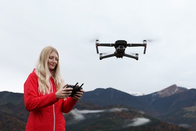 Young woman operating modern drone with remote control in mountains