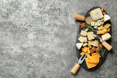 Cheese platter with specialized knives and fork on grey table, top view. Space for text