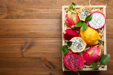 Delicious cut and whole dragon fruits in crate on wooden table, top view. Space for text