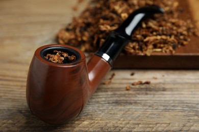 Smoking pipe with dry tobacco on wooden table, closeup