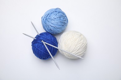 Soft woolen yarns with knitting needles on white background, top view