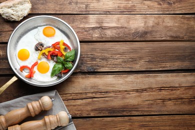 Tasty fried eggs with vegetables in pan and spice shakers on wooden table, flat lay. Space for text