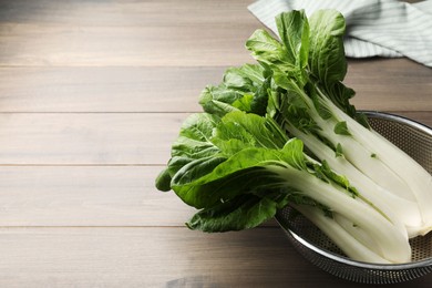 Photo of Fresh green pak choy cabbages in colander on wooden table, space for text
