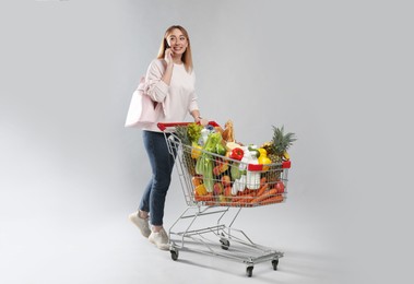 Young woman with shopping cart full of groceries talking on phone against grey background