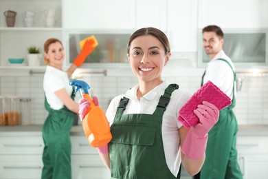 Portrait of young woman with sprayer and rag in kitchen. Cleaning service