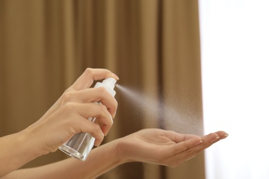 Woman spraying antiseptic onto hand indoors, closeup