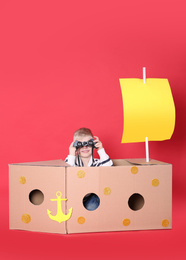 Little child playing with ship made of cardboard box on red background