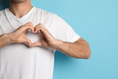Photo of Man making heart with hands on light blue background, closeup. Space for text