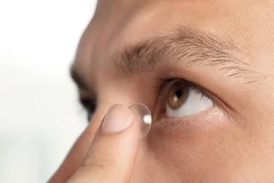 Man putting contact lens in his eye on white background, closeup