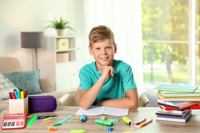 Cute boy doing homework at table with school stationery indoors