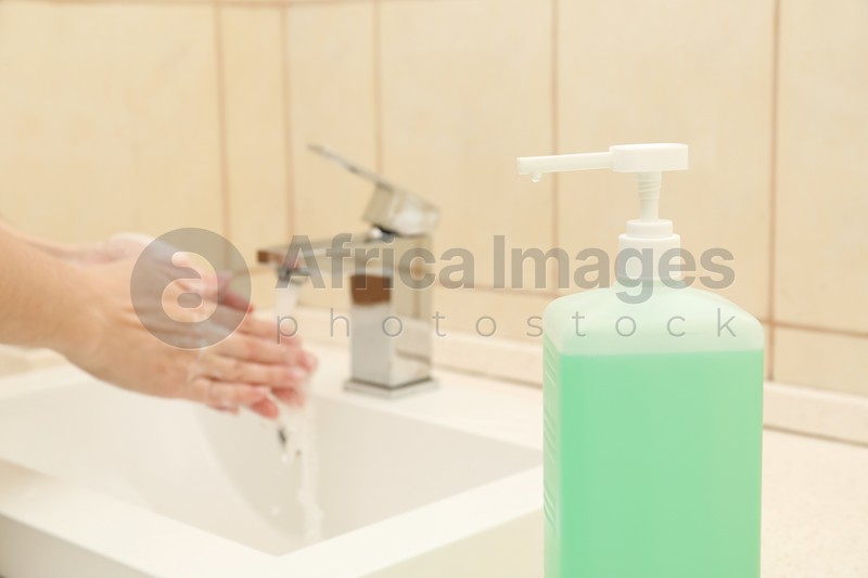 Woman washing hands in public bathroom, focus on antiseptic gel dispenser