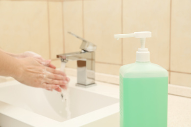 Photo of Woman washing hands in public bathroom, focus on antiseptic gel dispenser