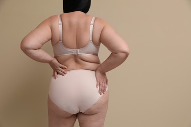 Back view of overweight woman in beautiful underwear on beige background, space for text. Plus-size model