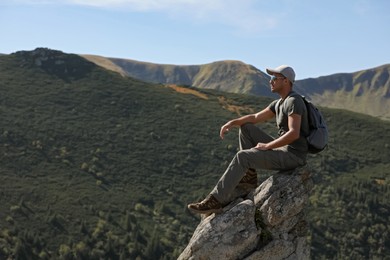 Tourist with backpack enjoying mountain landscape on rocky peak