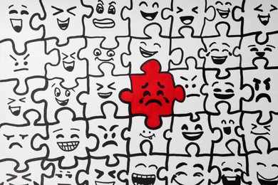 Photo of Drawing of white puzzle pieces and one red with different emotions, closeup. Bullying concept
