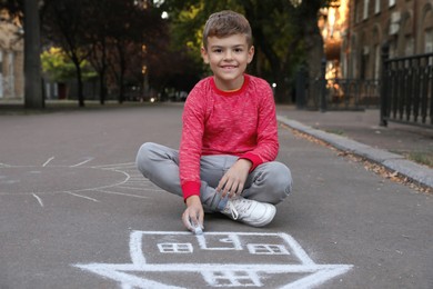 Child drawing house with chalk on asphalt