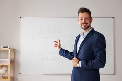 Photo of Happy teacher explaining mathematics at whiteboard in classroom